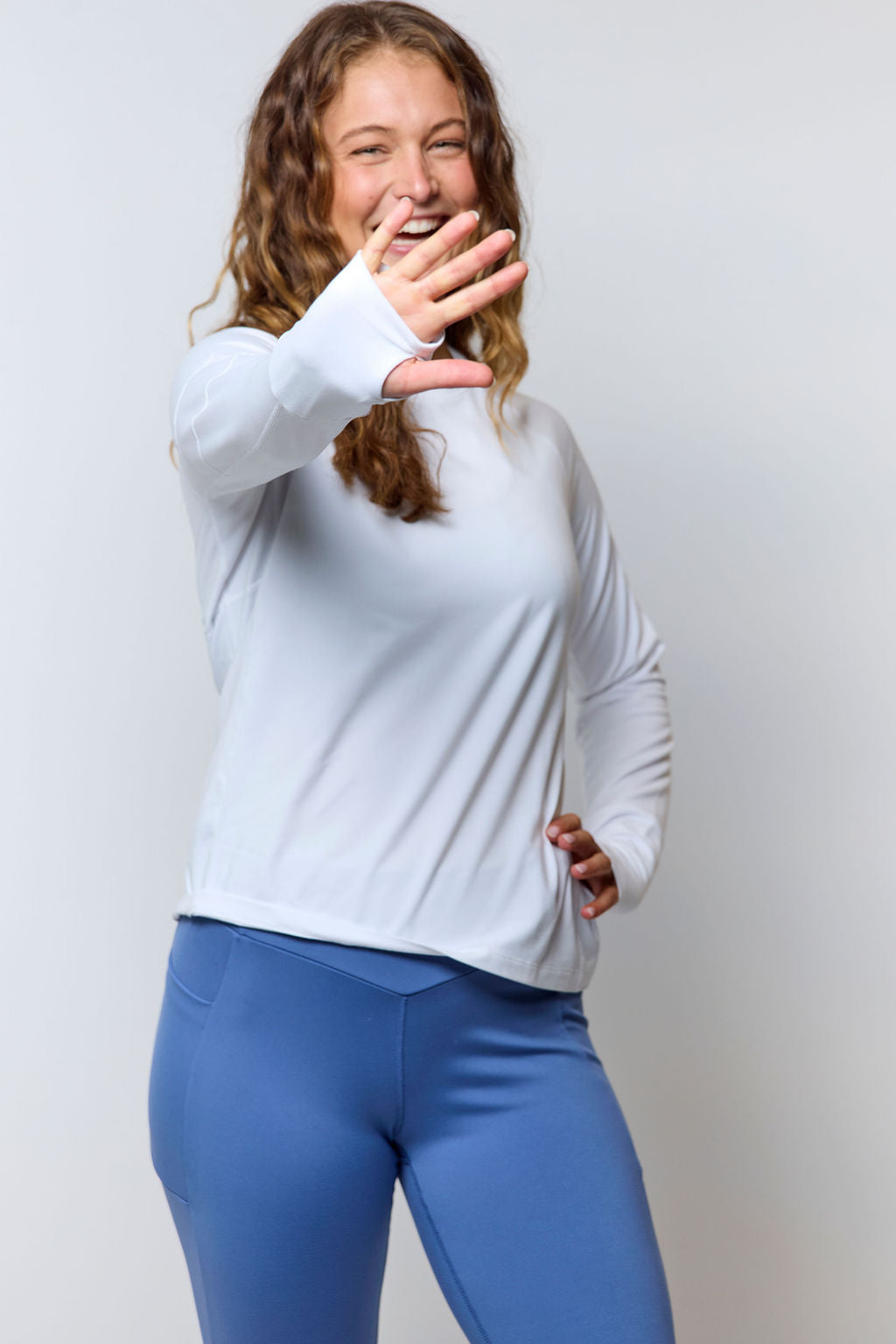 White Foudy 2.0 long-sleeve top, modeled with one hand raised and blue leggings