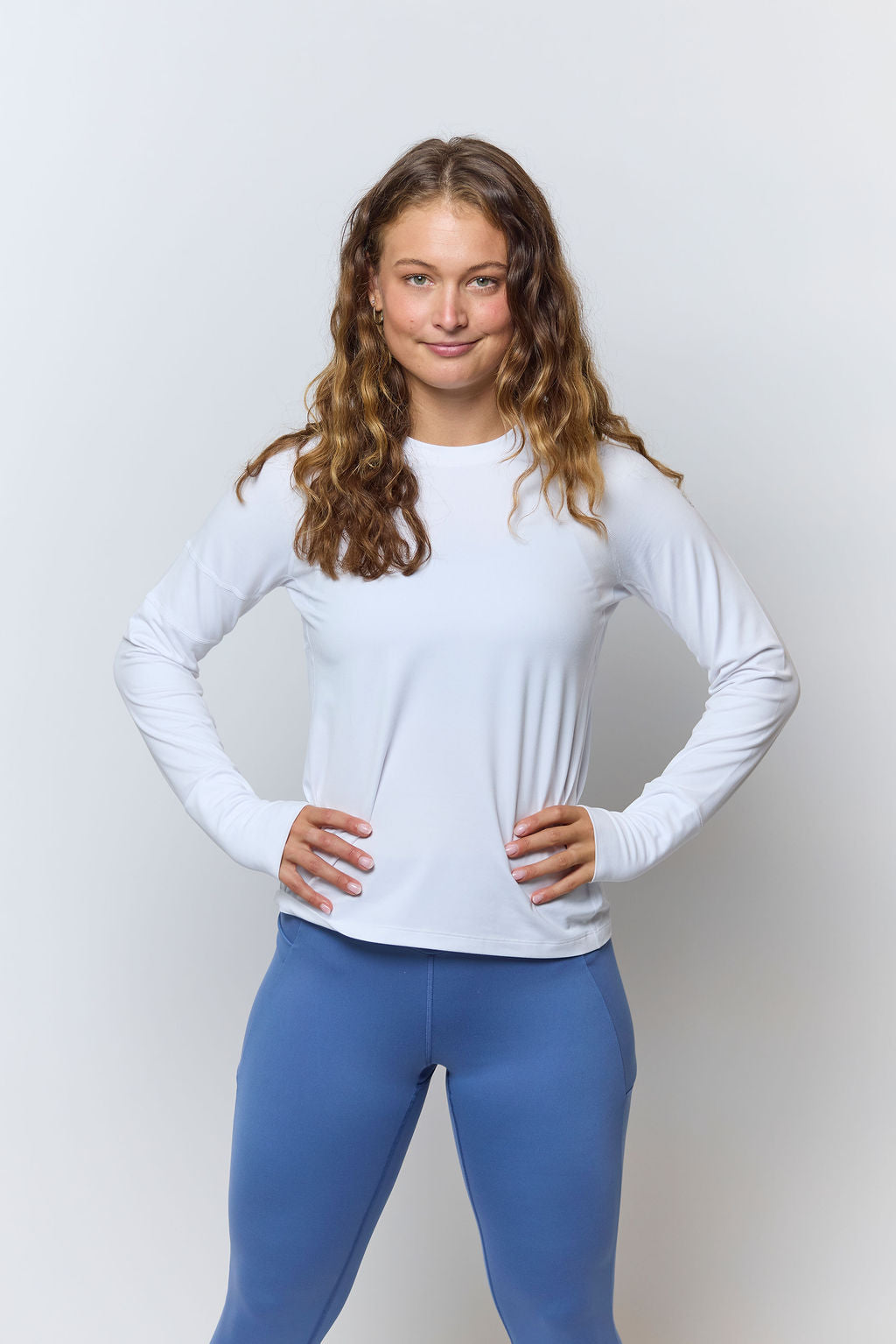 White Foudy 2.0 long-sleeve top, front view with hands on hips and blue leggings
