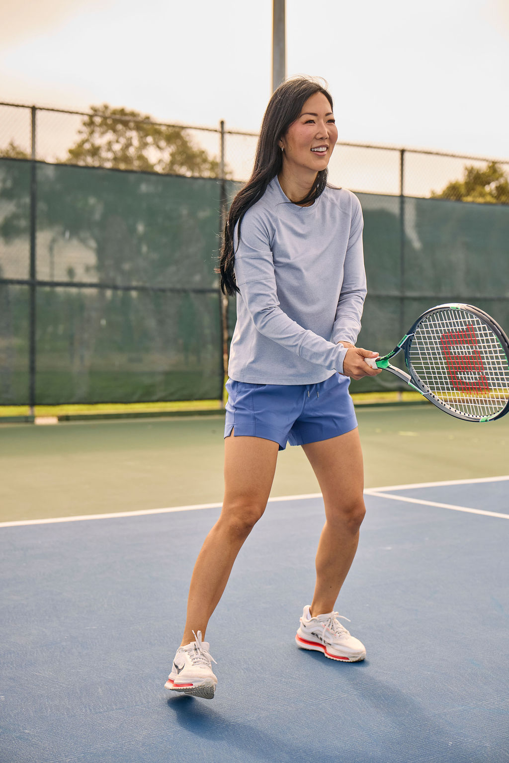 Woman wearing a light blue long-sleeve top and blue shorts, holding a racket on a tennis court