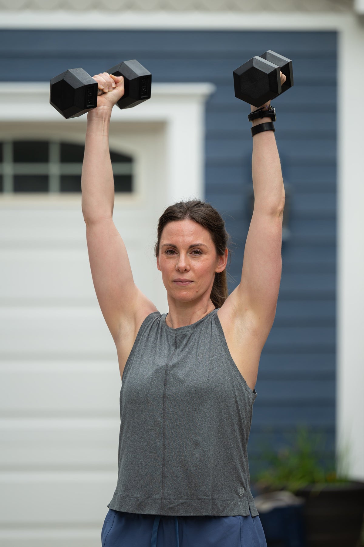 Gray Boxy Crop Tank, front view while lifting two dumbbells overhead outdoors