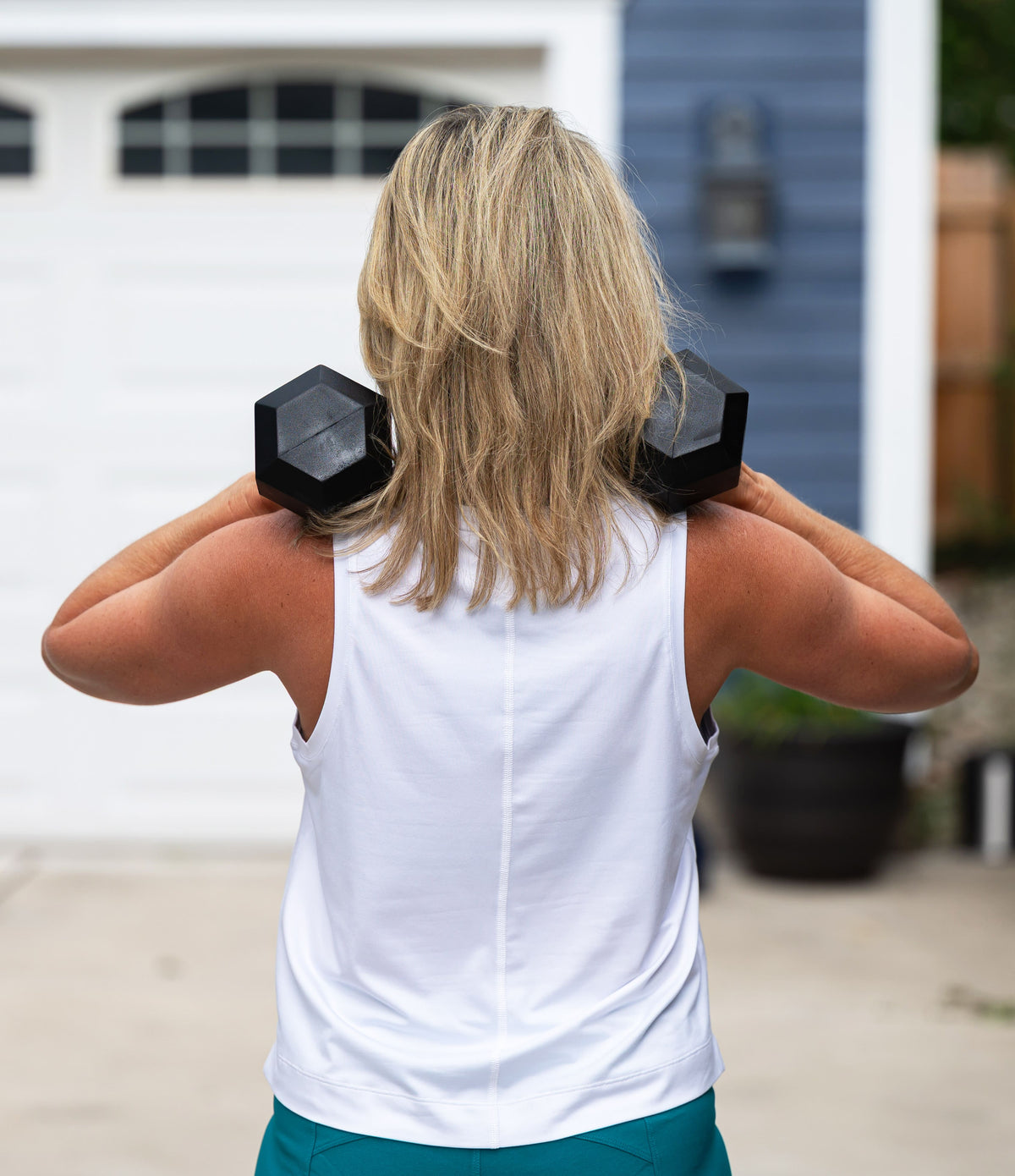 White Boxy Crop Tank, back view while holding dumbbells at the shoulders outdoors