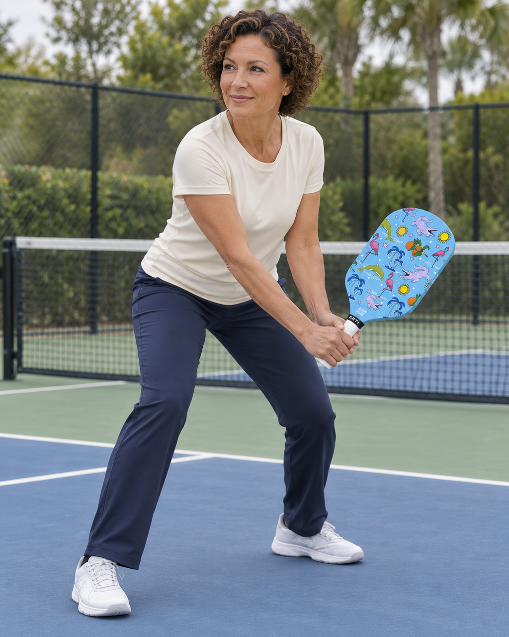 AI-assisted pickleball scene of one adult woman low backhand preparation using the blue ARTI FLORIDA paddle. Original supplier photos show product details.