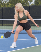 Adult woman in the Brushed Commit sports bra in Moss Ridge making a low forehand-side pickleball retrieval on an outdoor court; supporting gallery image.