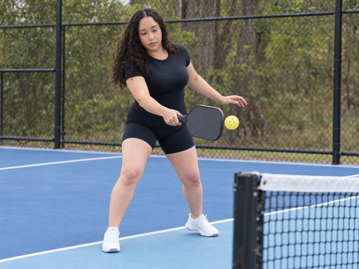 AI-assisted lifestyle image based on supplier photos; Black BRUSHED Commit tee shown during pickleball play