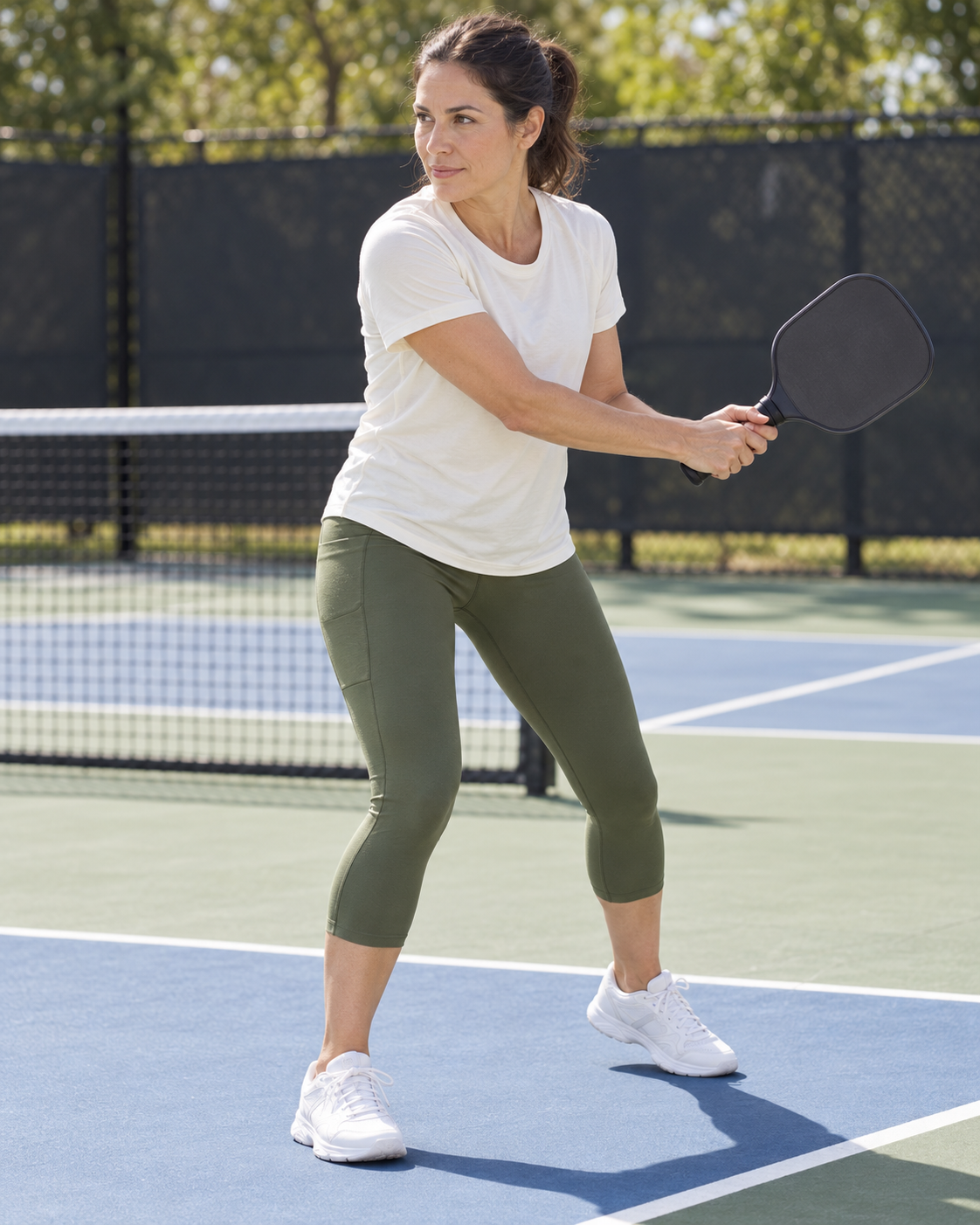AI-assisted image of an adult woman side profile backhand preparation wearing Go Again Women's Cropped Leggings Length 21" in Dark Moss.