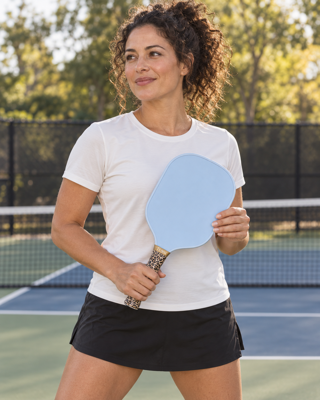 AI-assisted pickleball scene of one adult woman ready with a paddle wrapped in the leopard grip from TESSI Animal Lover. Original supplier photos show all three included grips.