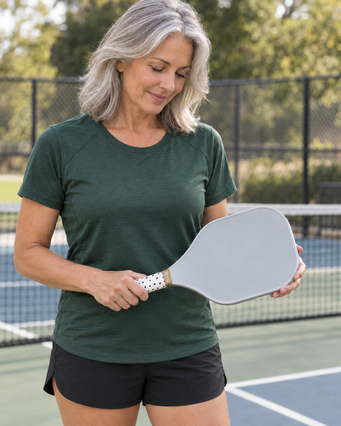 AI-assisted pickleball scene of one adult woman holding a paddle with the white/black polka-dot grip from TESSI Neutral Chic. Original supplier photos show all three included grips.